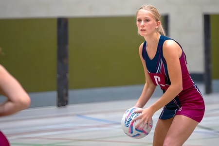 Eine Schülerin der Norwich School hält einen Volleyball auf dem Sportplatz mit grüner Wand im Hintergrund.