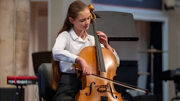 Eine Schülerin der Norwich School spielt Cello in einem Raum mit Holzvertäfelung und Musikinstrumenten im Hintergrund.