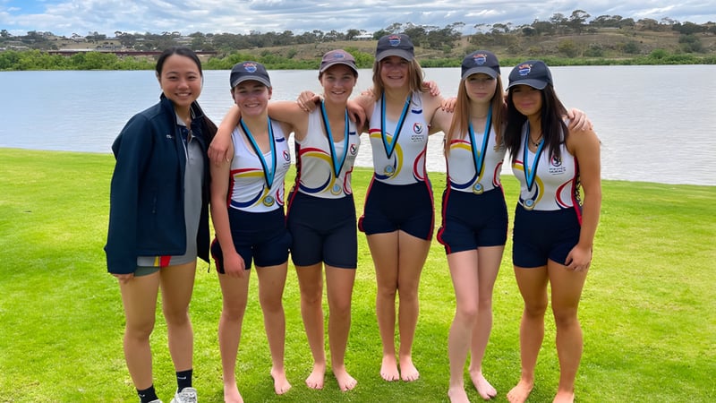 Eine Gruppe junger Athletinnen steht auf einem Rasenfeld nahe einem Gewässer auf dem Gelände der Norwood International High School.