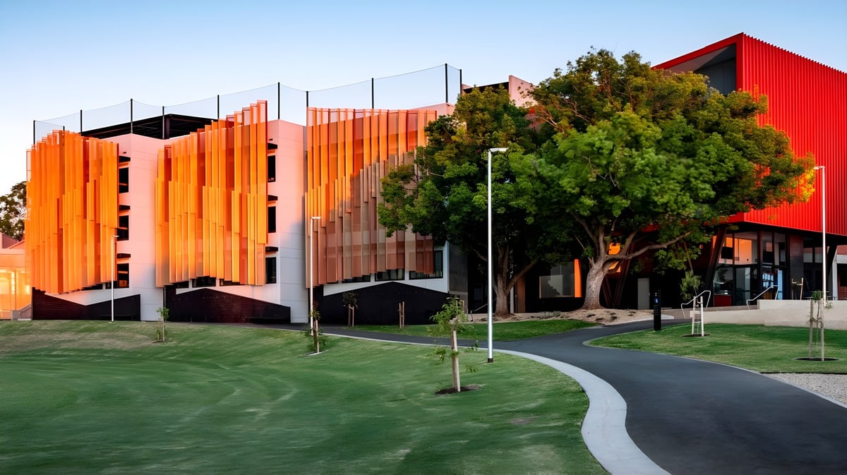 Das moderne Gebäude der Norwood International High School mit roten und orangefarbenen Fassaden in einer grünen Landschaft.