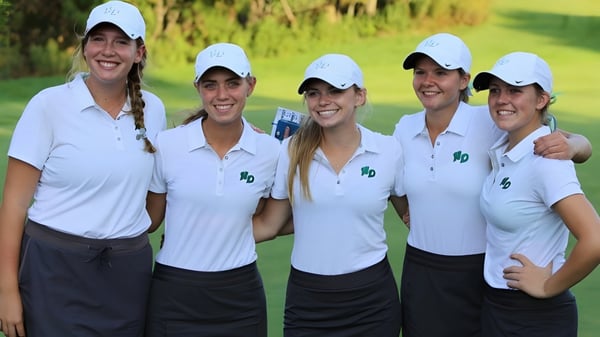 Eine Gruppe von fünf Schülerinnen in weißen Golfshirts steht auf einem Rasenfeld auf dem Campus der Notre Dame de la Baie Academy.