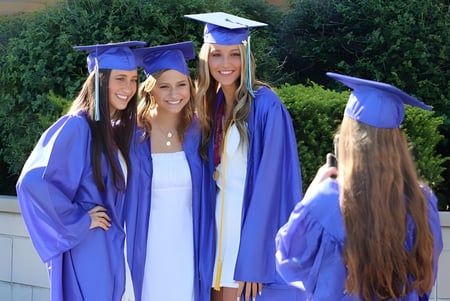 Vier Schülerinnen der Notre Dame de la Baie Academy in Abschlussgewändern stehen zusammen vor einem grünen Hintergrund.