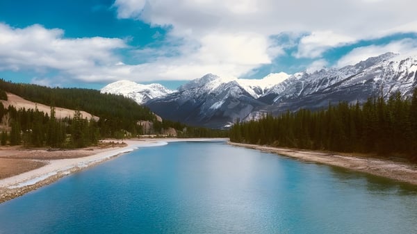 Ein ruhiger Fluss fließt durch eine Berglandschaft mit schneebedeckten Gipfeln nahe der Notre Dame High School in Calgary.