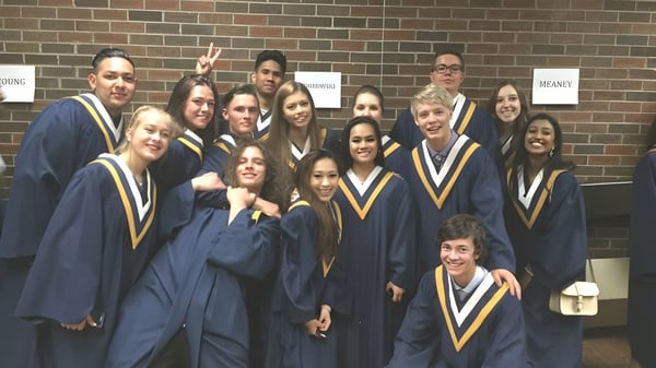 Eine Gruppe von Absolventinnen und Absolventen in der Abschlusskleidung der Notre Dame High School in Calgary posiert vor einer Backsteinwand.