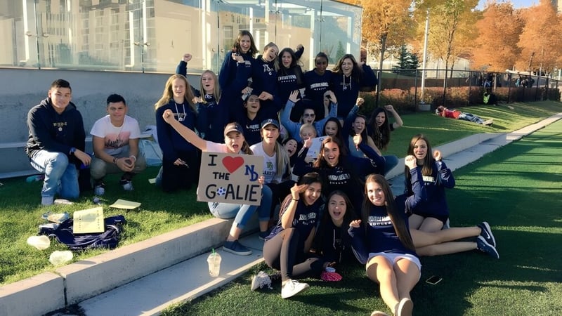 Eine Gruppe Schülerinnen und Schüler der Notre Dame High School in Calgary sitzt und steht auf einer Wiese vor einem Schulgebäude.