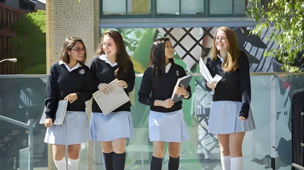 Eine Gruppe von Schülerinnen der Notre Dame High School steht vor einem Backsteingebäude mit großen Fenstern.
