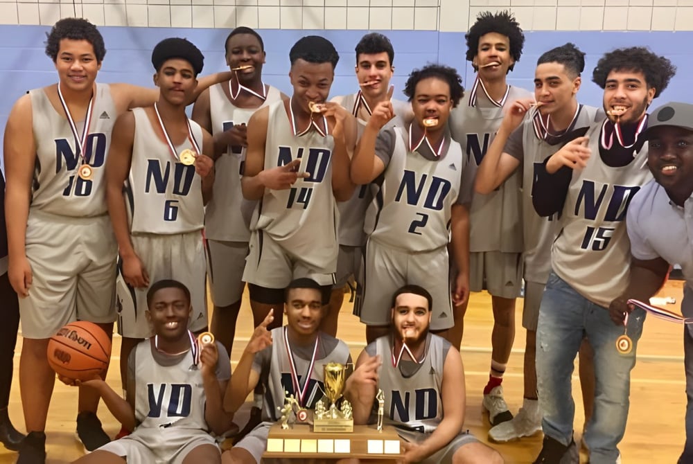 Eine Gruppe Schüler der Notre Dame High School feiert gemeinsam den Gewinn eines Basketball-Turniers mit einem Pokal.