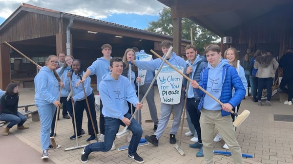 Eine Gruppe von Schülerinnen und Schülern der Notre Dame Saint Joseph steht mit blauen Hemden und Schildern vor einem Holzgebäude.