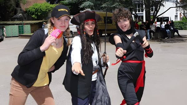 Drei Schülerinnen und Schüler stehen zusammen im Außenbereich der Notre Dame Saint Joseph Schule vor Gebäuden und Bäumen.