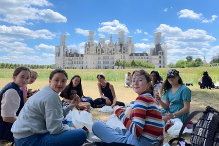 Eine Gruppe Schüler sitzt auf einer Wiese vor dem Schloss auf dem Gelände der Notre Dame Saint Joseph.