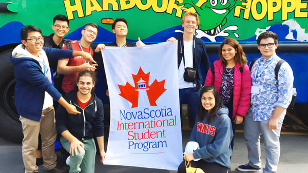 Schüler des Nova Scotia French Program stehen mit einem Banner vor dem farbenfrohen Harbour Hopper Wandbild.