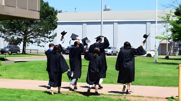 Eine Gruppe von Absolventen in schwarzen Talaren läuft auf dem Campus der Nova Scotia School über eine Wiese vor einem großen Gebäude.