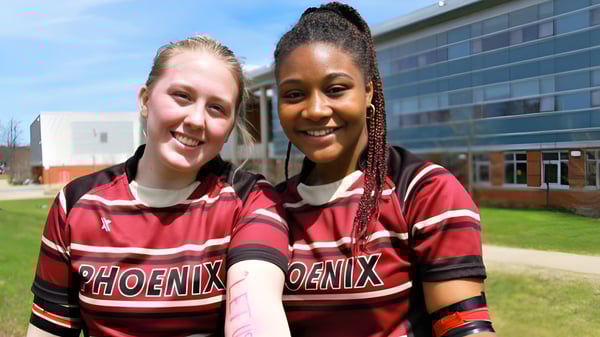 Zwei Schülerinnen der Nova Scotia School tragen passende Sporttrikots und stehen gemeinsam im Freien vor einem Gebäude.