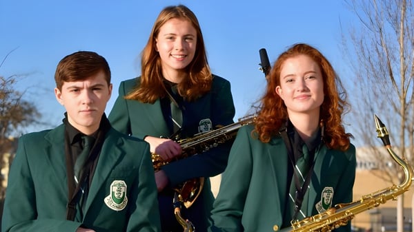 Drei Schüler der Oak Bay Secondary High School in grünen Uniformen stehen mit einem Saxophon und einer Trompete vor blauem Himmel und kahlen Bäumen.