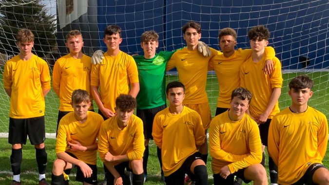Eine Gruppe von jungen Fußballspielern in gelben Trikots steht vor einem blauen Netz auf einem Rasenfeld auf dem Campus der Oak Leaf Studio.
