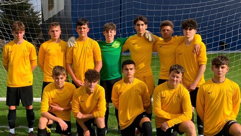 Eine Gruppe junger Fußballspieler in gelben Trikots posiert vor einem blauen Netz auf dem Sportplatz des Oak Leaf Studio.