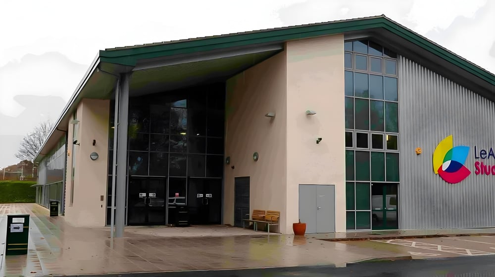 Das moderne mehrstöckige Gebäude des Oak Leaf Studio mit grünem Dach und großen Glasfenstern ist von einem gepflasterten Bereich umgeben.