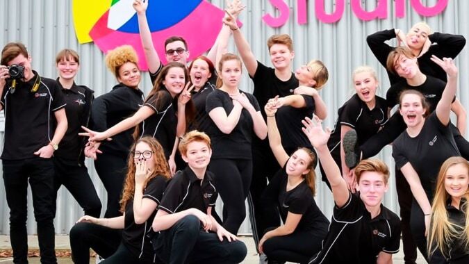 Eine Gruppe junger Schülerinnen in schwarzen Uniformen posiert vor einem farbenfrohen Studiohintergrund im Oak Leaf Studio.