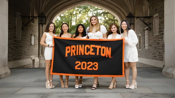 Eine Gruppe Schülerinnen der Oak Mountain Academy steht gemeinsam mit einem großen orangefarbenen Banner mit der Aufschrift PRINCETON 2023 unter einem malerischen Bogen.