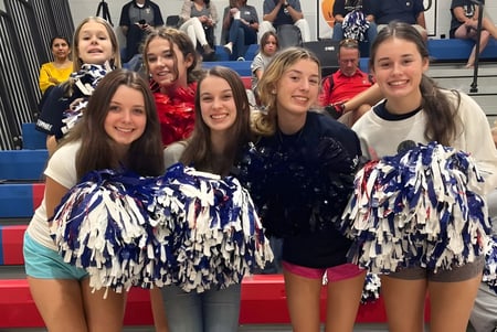 Eine Gruppe Cheerleader der Oak Mountain Academy posiert in bunten Uniformen mit einer Menschenmenge im Hintergrund.