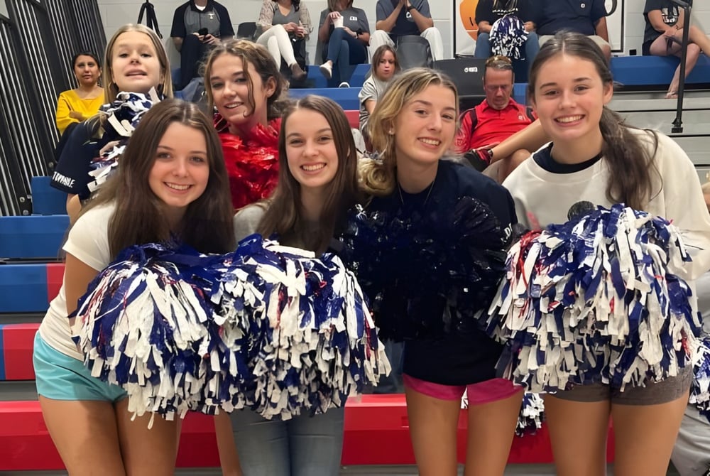 Eine Gruppe Cheerleader der Oak Mountain Academy posiert in bunten Uniformen mit einer Menschenmenge im Hintergrund.