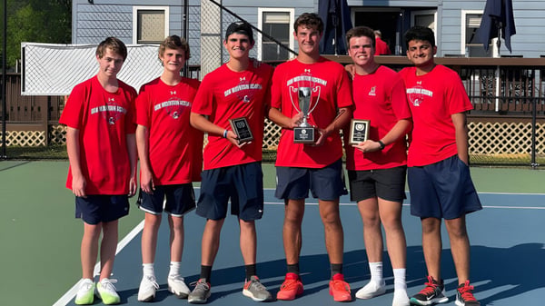 Eine Gruppe von Schülern der Oak Mountain Academy steht auf dem Tennisplatz und hält Pokale.