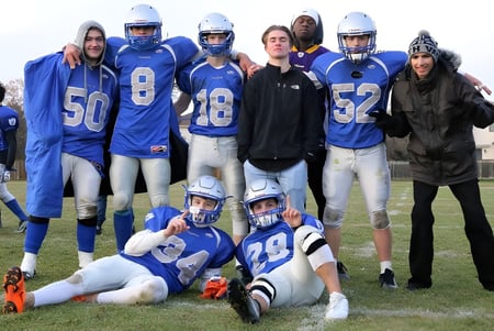 Eine Gruppe junger Fußballspieler in blauen Trikots auf dem Spielfeld der Oak Park High School mit Zuschauern im Hintergrund.