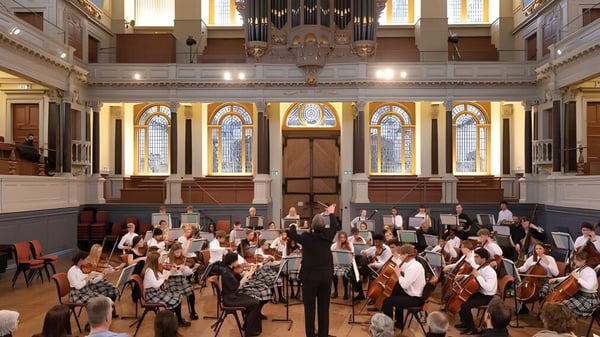 Ein Orchester spielt im Konzertsaal der Oakham School vor kunstvollen architektonischen Details und bunten Glasfenstern.
