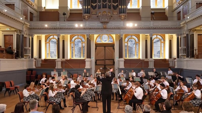 Ein Orchester spielt im Konzertsaal der Oakham School vor kunstvollen architektonischen Details und bunten Glasfenstern.