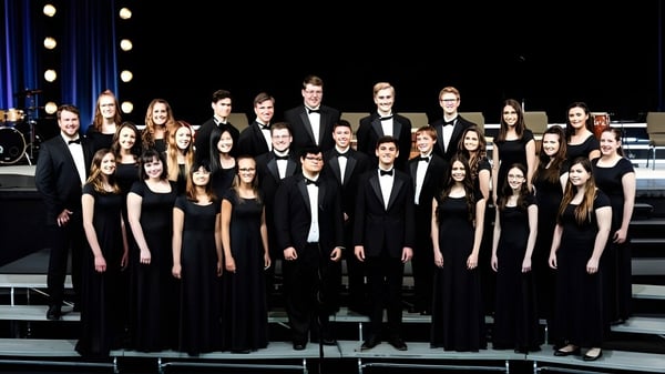 Eine große Gruppe von Schülerinnen und Schülern der Oakland Christian School steht formell gekleidet auf der Bühne unter Scheinwerfern.
