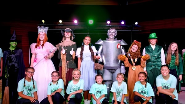 Schüler der Oakland Christian School stehen in Halloween-Kostümen auf einer Bühne mit bunter Beleuchtung.