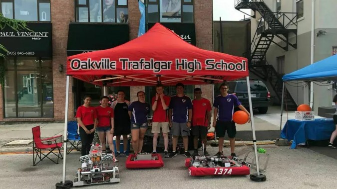 Schüler der Oakville Trafalgar High School stehen unter einem roten Zelt vor einem Backsteingebäude.