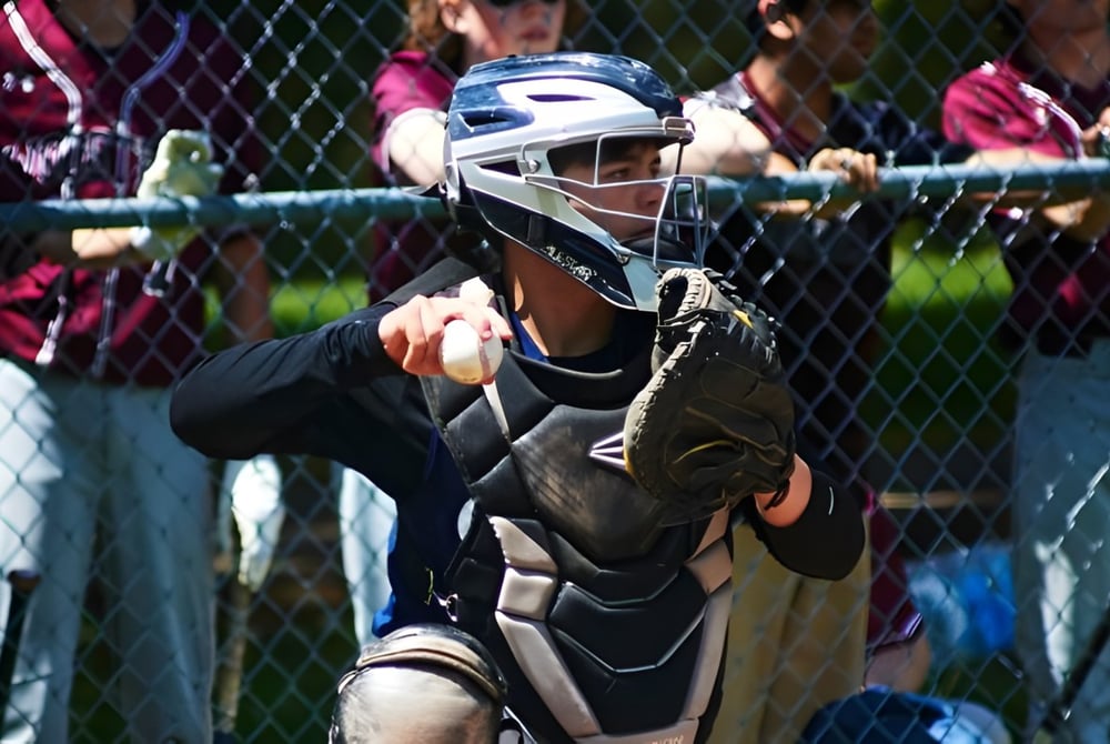Eine Person mit Baseball-Catcher-Maske steht hinter einem Drahtzaun auf dem Gelände der Oakwood Friends School.