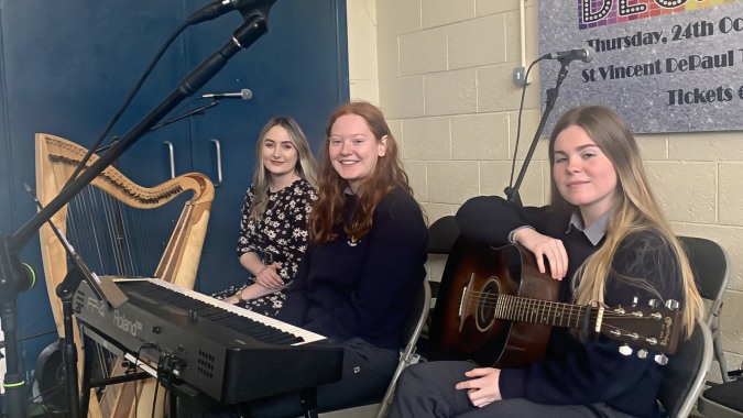 Drei Schülerinnen des O’Carolan College spielen auf der Bühne Harfe und Gitarren bei einem Auftritt.