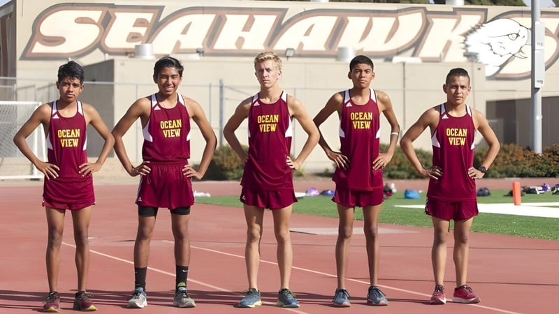 Fünf junge Athleten in roten Trikots stehen auf der Sportbahn der Ocean View High School vor einem großen SEAHAWK-Schild.