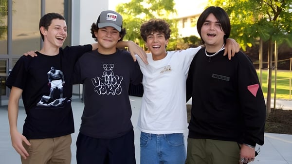 Vier Schüler der Ojai Valley School stehen im Freien und lächeln vor einem Gebäude mit Bäumen.
