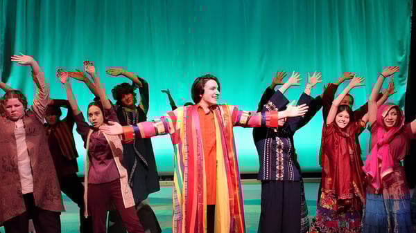 Eine Gruppe von Schülerinnen und Schülern der Okanagan Mission Secondary School führt auf einer Bühne mit grünem Hintergrund auf.