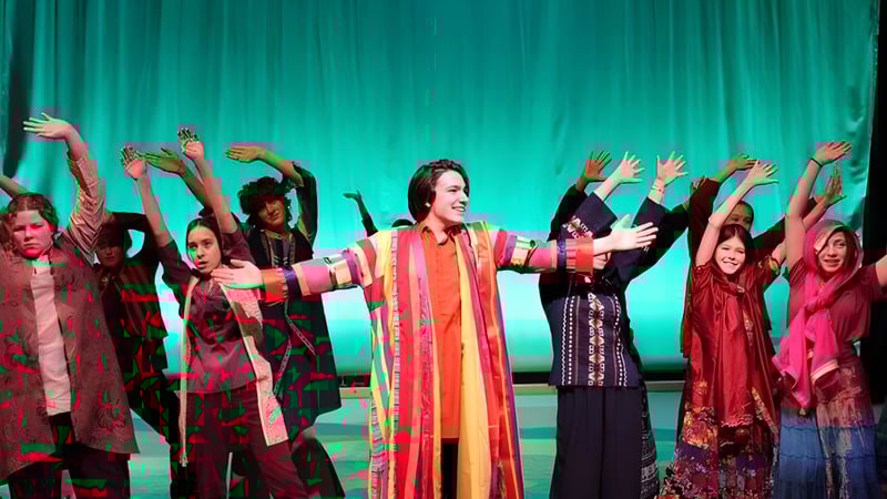 Eine Gruppe von Schülerinnen und Schülern der Okanagan Mission Secondary School führt auf einer Bühne mit grünem Hintergrund auf.