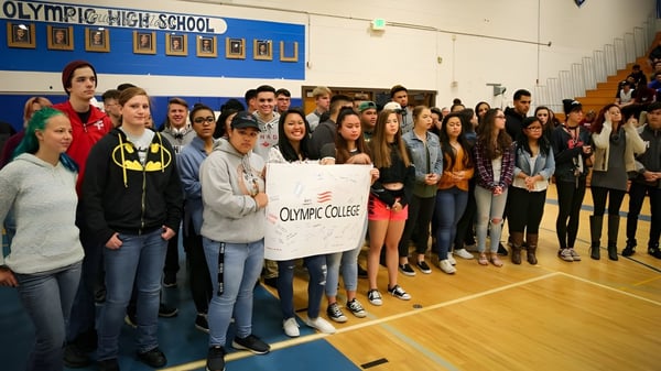 Eine Gruppe von Schülern des Olympic College versammelt sich in der Turnhalle und hält ein Schild mit dem Namen der Schule.