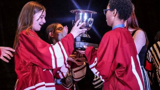 Schüler der École secondaire publique Omer-Deslauriers feiern mit einer Trophäe in einem schwach beleuchteten Raum.