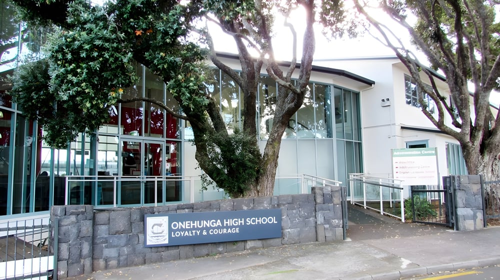 Das Steinschild der Onehunga High School steht vor einem modernen Gebäude und umgeben von grüner Vegetation.