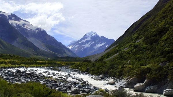 Eine verschneite Bergkette ist hinter grüner Vegetation und einem Bach auf dem Gelände des Onslow College zu sehen.