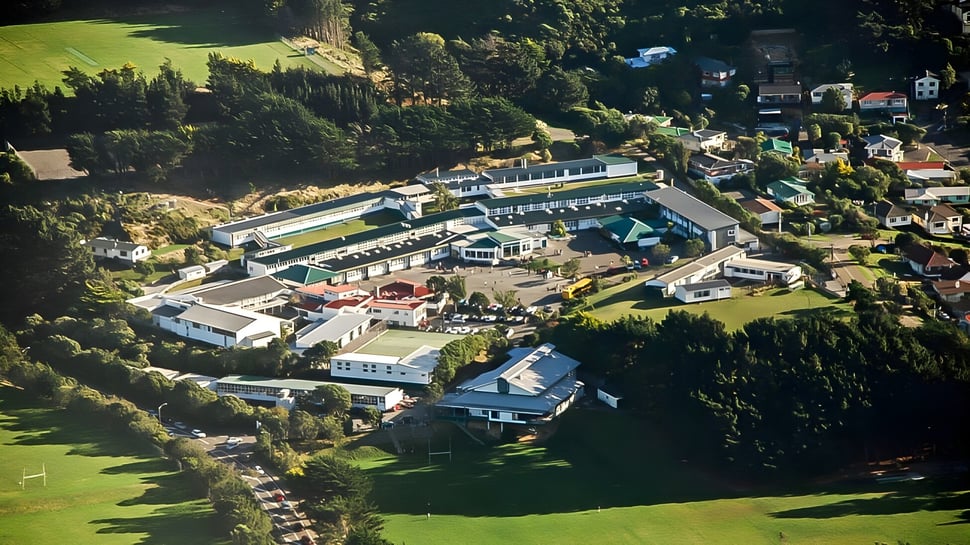 Luftaufnahme des Onslow College Campus mit mehreren Gebäuden, Schwimmbädern und viel Grün umgeben von bewaldeten Hügeln.