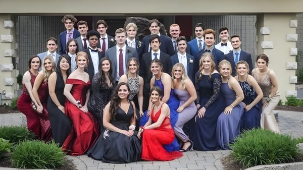 Eine Gruppe formal gekleideter Personen posiert im Außenbereich der Ontario Hockey Academy auf einem gepflasterten Weg mit Grünflächen im Hintergrund.