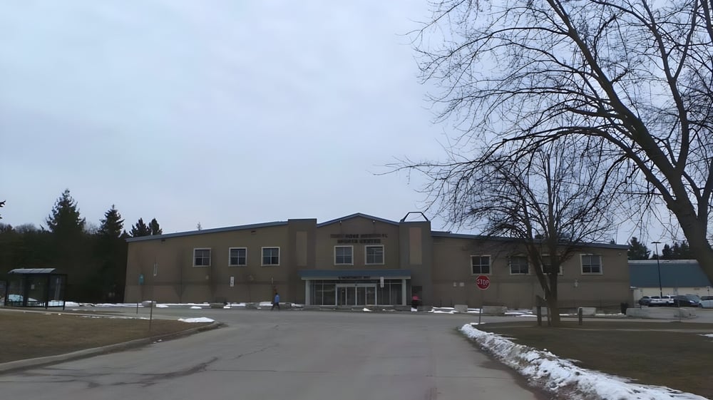 Das zweistöckige Gebäude der Orangeville District Secondary School steht vor einer verschneiten Landschaft mit kahlen Bäumen.