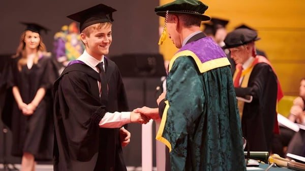 Zwei Absolventen in Talaren schütteln sich die Hand bei der Abschlussfeier der Orangeville District Secondary School.