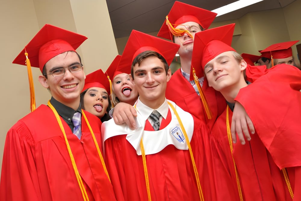 Eine Gruppe von Absolventen der Orangewood Christian School posiert in roten Talaren zusammen vor einem schlichten Hintergrund.