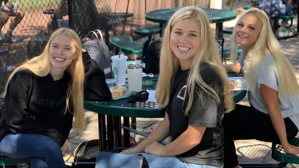 Drei Schülerinnen mit langen blonden Haaren sitzen an einem Tisch im Freien auf dem Campus der Orangewood Christian School.