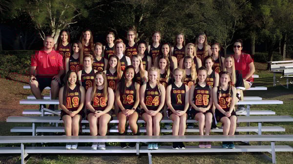 Eine Gruppe junger Sportlerinnen der Orangewood Christian School sitzt auf Tribünen im Freien vor Bäumen.