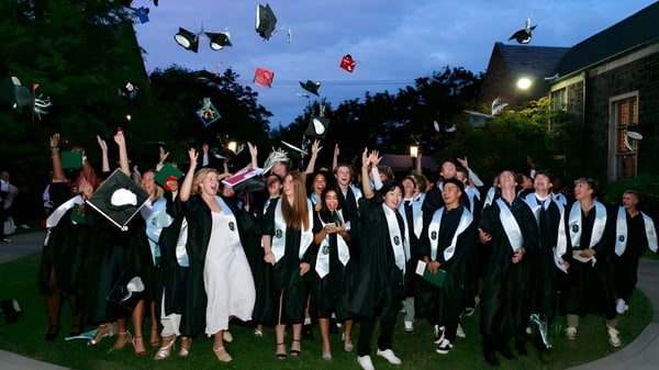 Eine Gruppe von Absolventinnen und Absolventen der Oregon Episcopal School steht abends im Freien in akademischer Kleidung zusammen.